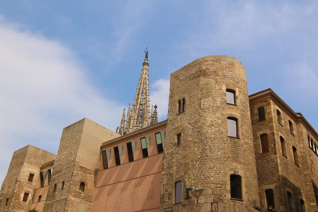 Historic stone towers and Gothic architecture stand alongside modern additions in Barcelona’s Gothic Quarter, with the spire of Barcelona Cathedral visible in the background.