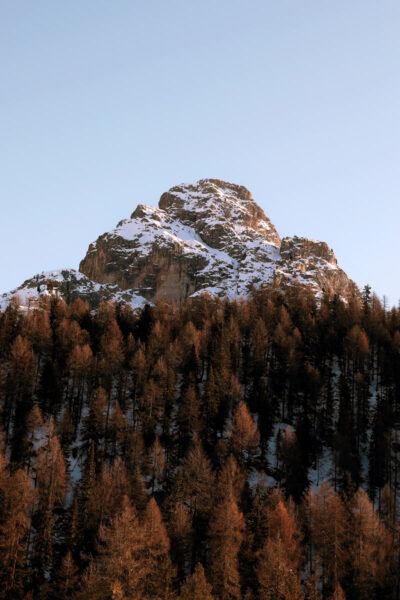 Beautiful autumnal photo of a snow-capped mountain of the Dolomites, Italy surrounded by reddish trees taken by Photographer Scott Allen Wilson.