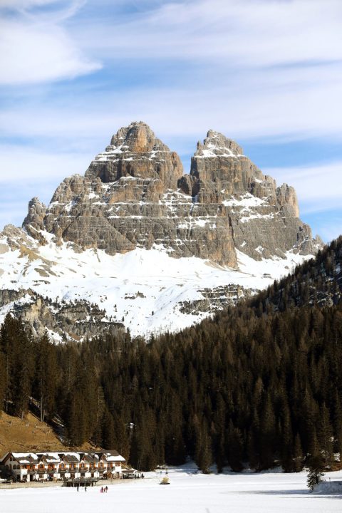 Beautiful landscape photography of the tall Dolomites mountain range in Italy with a forest and houses below, taken by Photographer Scott Allen Wilson.