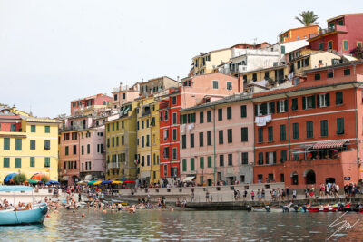 Multicolored buildings facing the sea and beachgoers enjoying a sunny day in Vernazza, Cinque Terre. By Photographer Scott Allen Wilson.