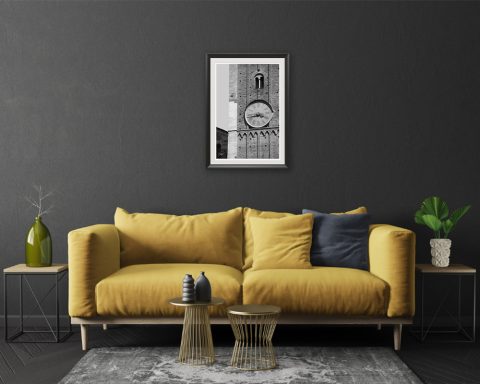 A black and white print of a clock tower of Parma hung in a dark living room with a yellow sofa and house plants. By Photographer Scott Allen Wilson.