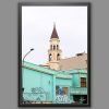 A black framed print of a clock tower emerging from the back of a bright turquoise building covered in graffiti in Pescara, Italy. By Photographer Scott Allen Wilson.
