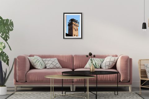 A black framed print of Torre Guinigi with trees on top of it in Lucca, Italy, hanging in a minimal living room. By Photographer Scott Allen Wilson.