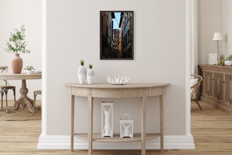 A dark brown framed print of Torre Guinigi in Lucca, Italy, hanging in a modern room with minimal wooden furniture. By Photographer Scott Allen Wilson.