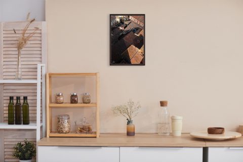 A dark brown framed print of red tiled rooftops in Lucca, Italy, hanging in a minimal room with wooden decor. By Photographer Scott Allen Wilson.