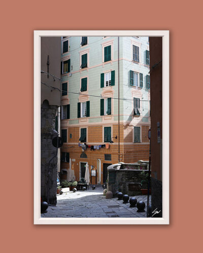White framed artistic print of a gorgeous alley in Genova, Italy, showcasing the vibrant colors of a building along a downhill cobblestone street. Photo captured by Travel Photographer Scott Allen Wilson.