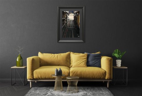The dove grey walls of this living room merge with the colors of the frame and the street, amplifying the space within the image, while a bright yellow couch matches the details of the road stripes and the sunlit facades, producing an exquisite contrast.