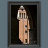 Beckoning by Scott Allen Wilson – framed fine art print of a sunlit medieval brick tower framed by a dark Gothic arch, Cremona, displayed in a black frame on a grey background