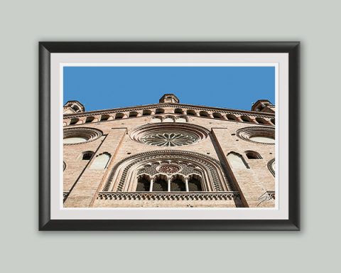 Fine art framed print of an ornate Romanesque facade with a rose window and intricate stone carvings against a blue sky, Looking to the East by Scott Allen Wilson, available in 8x12 and 16x24.