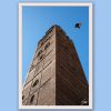 Fine art framed print of a dramatic low-angle view of a towering historic brick structure with a bird in flight against a deep blue sky, The Brick Roost by Scott Allen Wilson, available in 8x12 and 16x24.