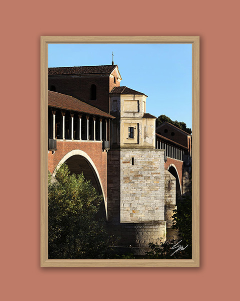 Framed travel art print of Pavia’s historic covered bridge captured in warm evening light.