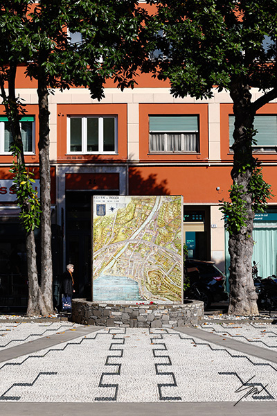 Fine art photograph of the historic map of Recco framed by trees and the town's colorful architecture in Liguria, Italy.