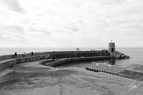 Black and white fine art photograph of Recco Harbour displayed in a black frame on a living room wall, featuring the curved breakwater and lighthouse in Italy.