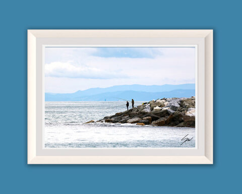 Framed fine art print depicting a quiet coastal morning with fishermen on a stone jetty, calm sea, and layered mountains in the distance.