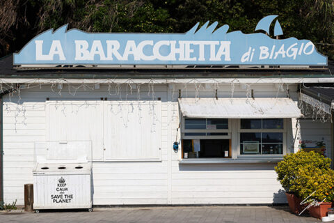 Historic white beach kiosk with the blue "La Baracchetta di Biagio" sign, photographed on the Ligurian coast in Italy.