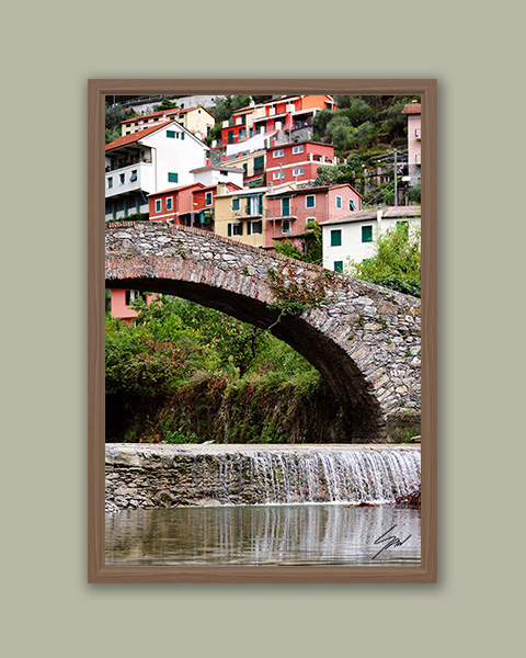 Fine art photograph of Recco's historic Roman bridge with colorful hillside homes and cascading water below.