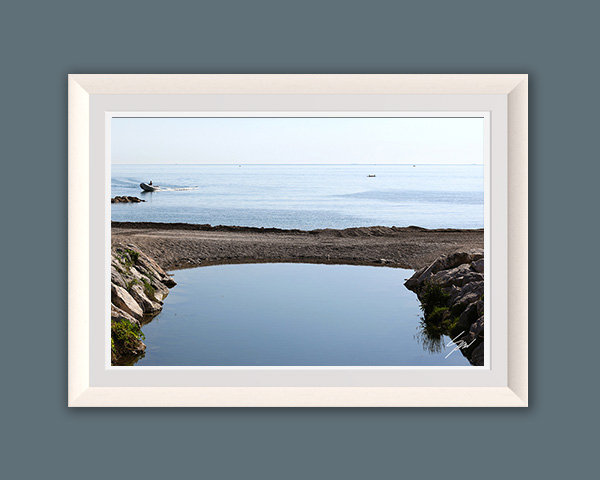Peaceful coastal scene in Recco, Italy, where a still tidal pool mirrors the sky as a small boat glides across the Ligurian Sea.