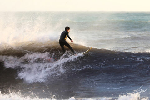 Travel fine art photography wall art featuring a lone surfer riding an ocean wave, bringing movement and energy to any space.