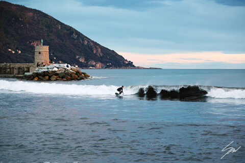 Framed fine art photography print of a surfer riding a wave near the historic tower in Recco, Italy, displayed in a surf shop.