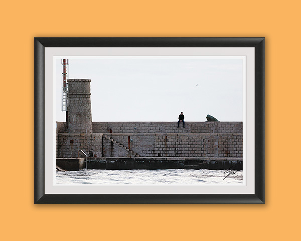 Framed travel photography print featuring a lone figure on the Recco harbor wall with the lighthouse tower and Ligurian Sea.