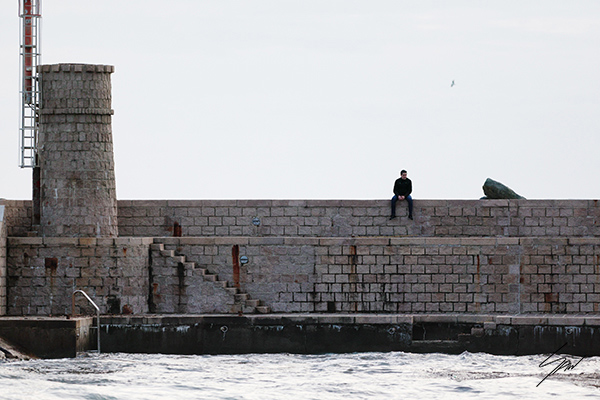 Framed travel photography print featuring a lone figure on the Recco harbor wall with the lighthouse tower and Ligurian Sea.