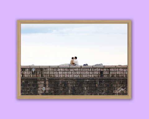 Fine art photograph of two people sitting together atop the stone breakwater overlooking the sea in Recco, Italy.