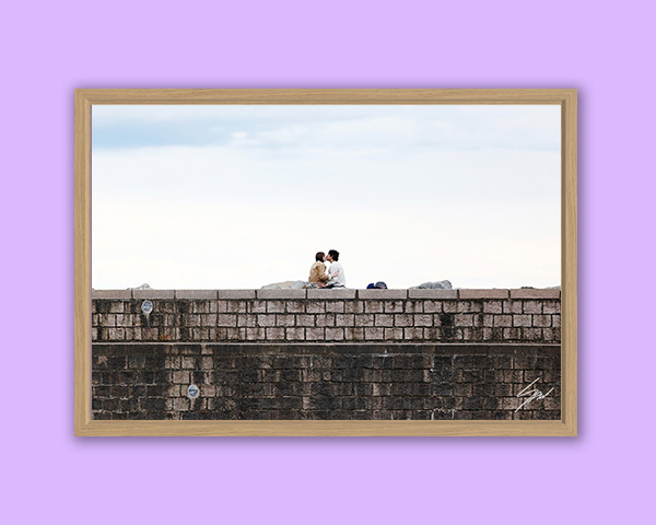 Fine art photograph of two people sitting together atop the stone breakwater overlooking the sea in Recco, Italy.