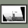 Monochrome coastal photography print featuring a Coast Guard aircraft passing above a stone lighthouse, creating a striking blend of maritime history and aviation.