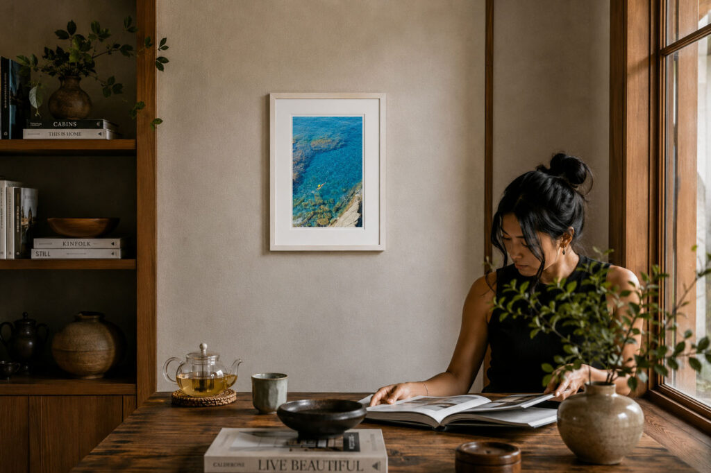 Framed fine art photograph of a lone swimmer floating in crystal-clear turquoise water displayed in a warm, minimalist reading space.