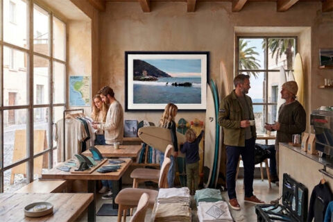Framed fine art photography print of a surfer riding a wave near the historic tower in Recco, Italy, displayed in a surf shop.